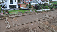 Eine Straße durch ein Wohngebiet ist aufgegraben und man sieht die Mauern eines antiken Hauses.